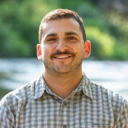 Headshot of Daniel Rothberg standing outside and smiling wearing a button up shirt