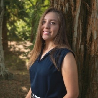 Image of Diana Rodriguez leaning against a tree in a forest