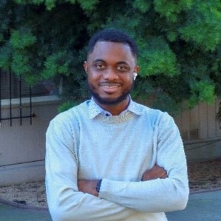 Photo of Isaac Frimpong smiling with his arms crossed and standing in front of a tree
