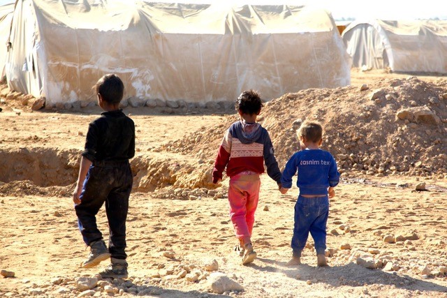 Three children walking through a refugee camp in Jordan