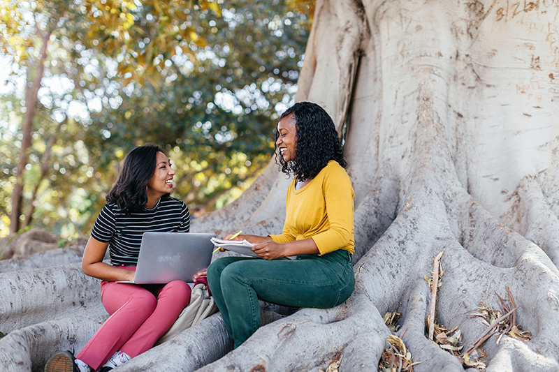 Two UCI students sitting on the roots of a tree