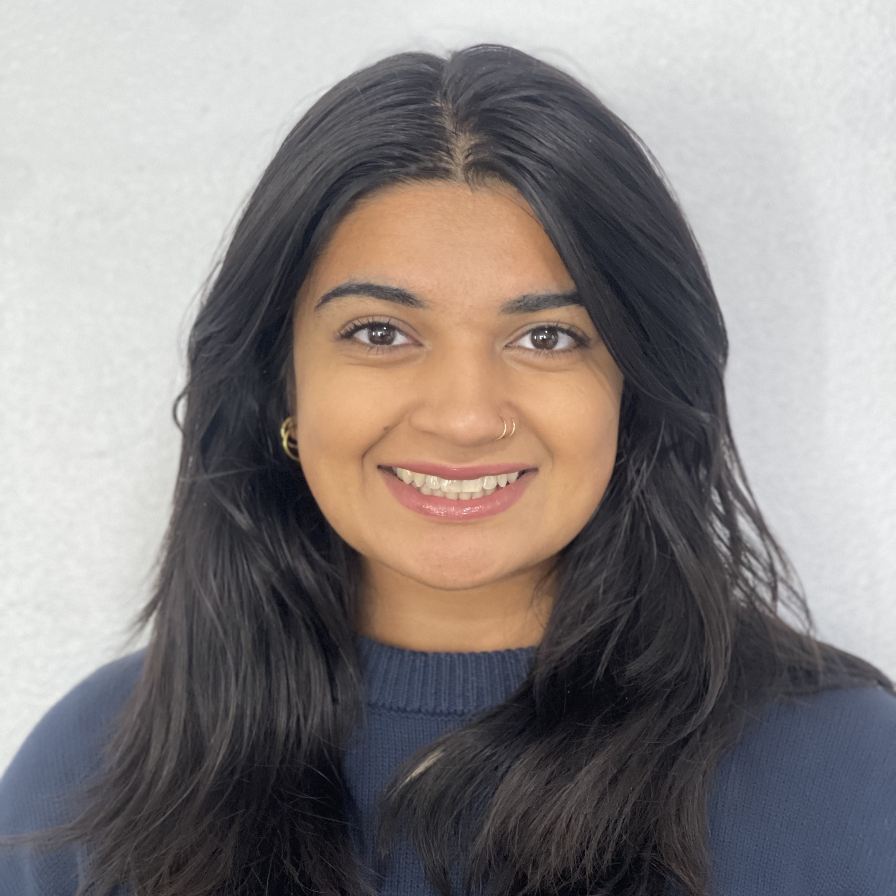 A smiling woman with long black hair and hoop earrings against a light gray background.