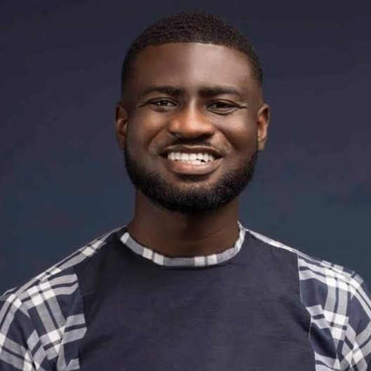 A smiling young man with a beard dressed in a stylish plaid shirt.