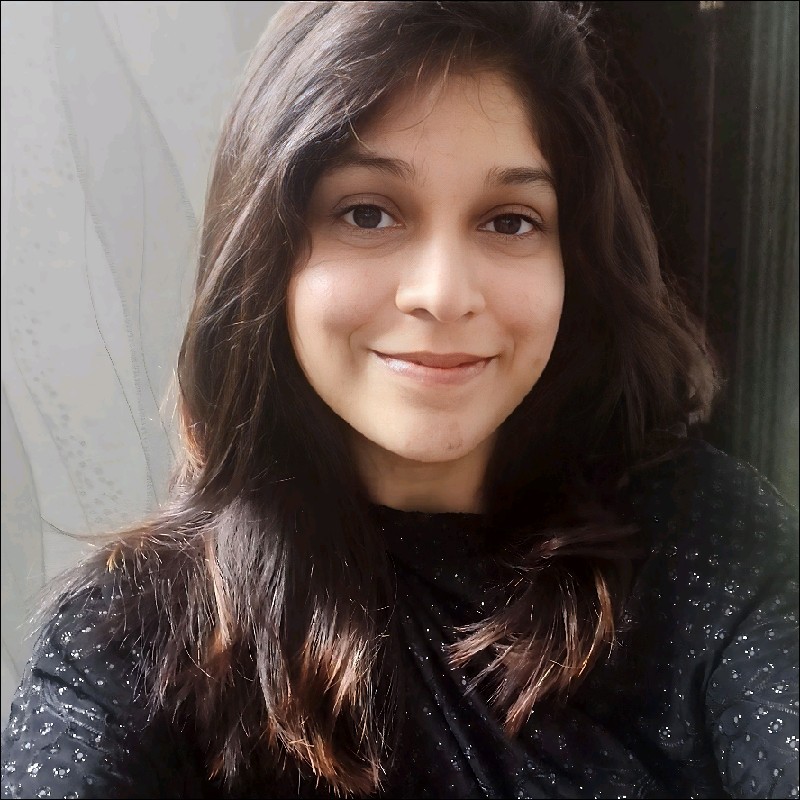 A smiling woman with long, dark hair, wearing a black outfit, posing for a close-up selfie.